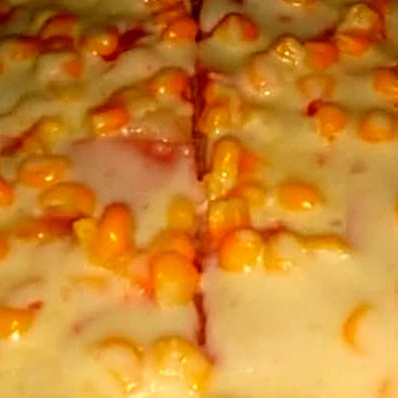 Granos de maíz sobre queso fundido en una pizza Maizito